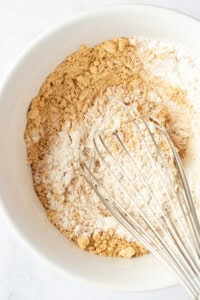 Top view of a mixing bowl containing flour and brown sugar with a metal whisk resting inside.