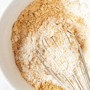 Top view of a mixing bowl containing flour and brown sugar with a metal whisk resting inside.