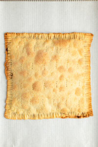 A baked, rectangular pie with crimped edges, small perforations on the top, and a golden-brown crust, placed on parchment paper.