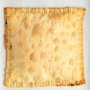 A baked, rectangular pie with crimped edges, small perforations on the top, and a golden-brown crust, placed on parchment paper.