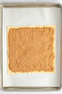 Rectangular dough on parchment paper with a layer of brown sugar filling spread evenly on top.
