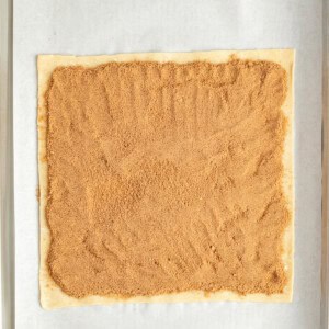 Rectangular dough on parchment paper with a layer of brown sugar filling spread evenly on top.