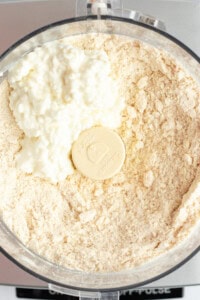 A food processor bowl filled with flour and cottage cheese.