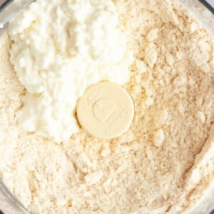 A food processor bowl filled with flour and cottage cheese.