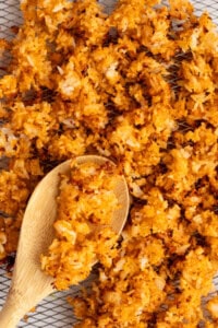 Close-up of crispy, golden-brown fried rice scattered on a wire rack with a wooden spoon.