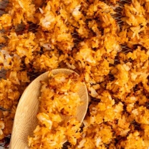 Close-up of crispy, golden-brown fried rice scattered on a wire rack with a wooden spoon.