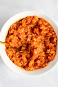 A bowl of chopped peach chutney with a golden spoon on a light surface.