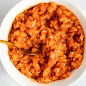 A bowl of chopped peach chutney with a golden spoon on a light surface.