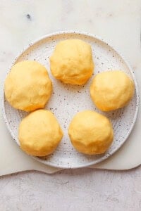 Five yellow dough balls on a speckled plate placed on a light surface.