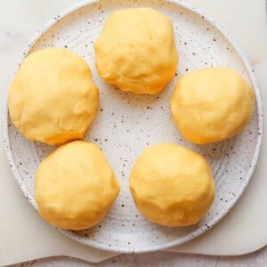 Five yellow dough balls on a speckled plate placed on a light surface.