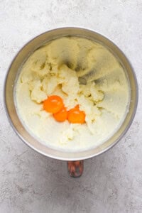 Mixing bowl with creamed butter and sugar, and two egg yolks on top, on a textured surface.