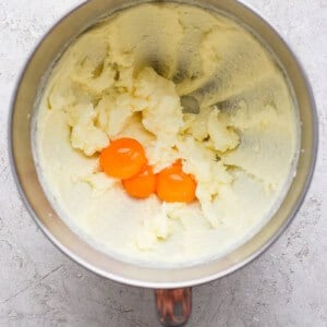 Mixing bowl with creamed butter and sugar, and two egg yolks on top, on a textured surface.