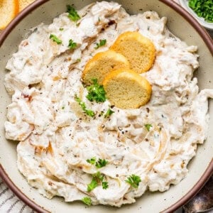 A bowl of creamy dip garnished with herbs and three round crackers on top.