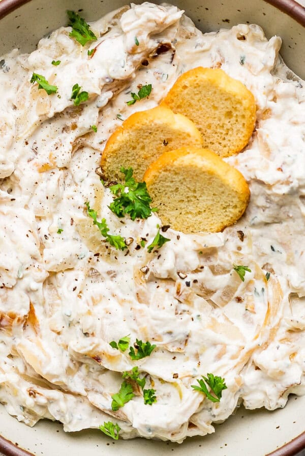 A bowl of creamy dip garnished with herbs and three round crackers on top.