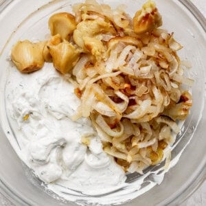 A bowl contains roasted garlic, caramelized onions, and herb-infused creamy dip.