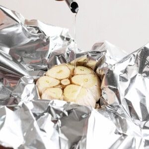 Oil being poured onto a halved garlic bulb placed on aluminum foil.