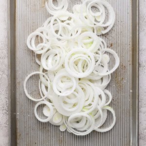 Thinly sliced onion rings spread on a baking sheet with a textured surface.