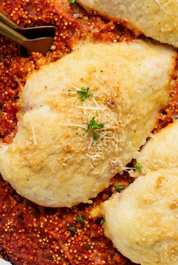 Baked chicken breasts with cheese on a bed of tomato sauce, garnished with parsley and grated cheese, in a white dish.