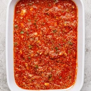 Close-up of a white baking dish filled with red tomato sauce mixed with visible herbs and spices.