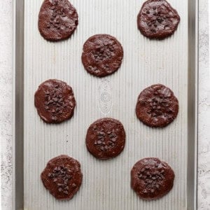 Unbaked chocolate cookies arranged on a baking sheet, topped with chocolate chips.