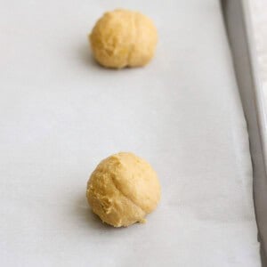 Two balls of lemon cookie dough placed on a parchment-lined baking sheet, destined for a sweet finish with cream cheese frosting.