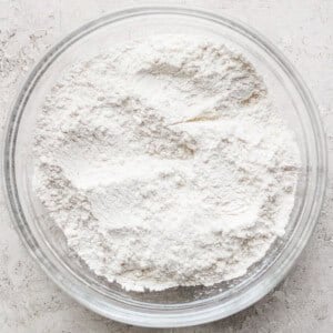 A clear glass bowl filled with white flour rests on a textured gray surface, ready for crafting delicious lemon cookies with cream cheese frosting.