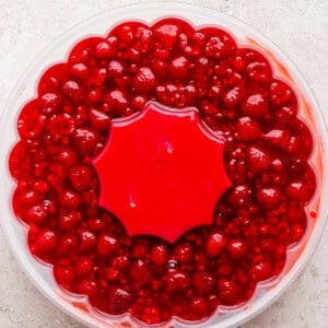 A clear plastic container filled with bright red cherry compote, featuring a red star-shaped lid in the center.