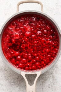 Top view of a pot containing a bubbling red sauce with visible fruit chunks.