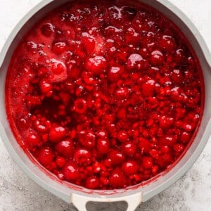 Top view of a pot containing a bubbling red sauce with visible fruit chunks.