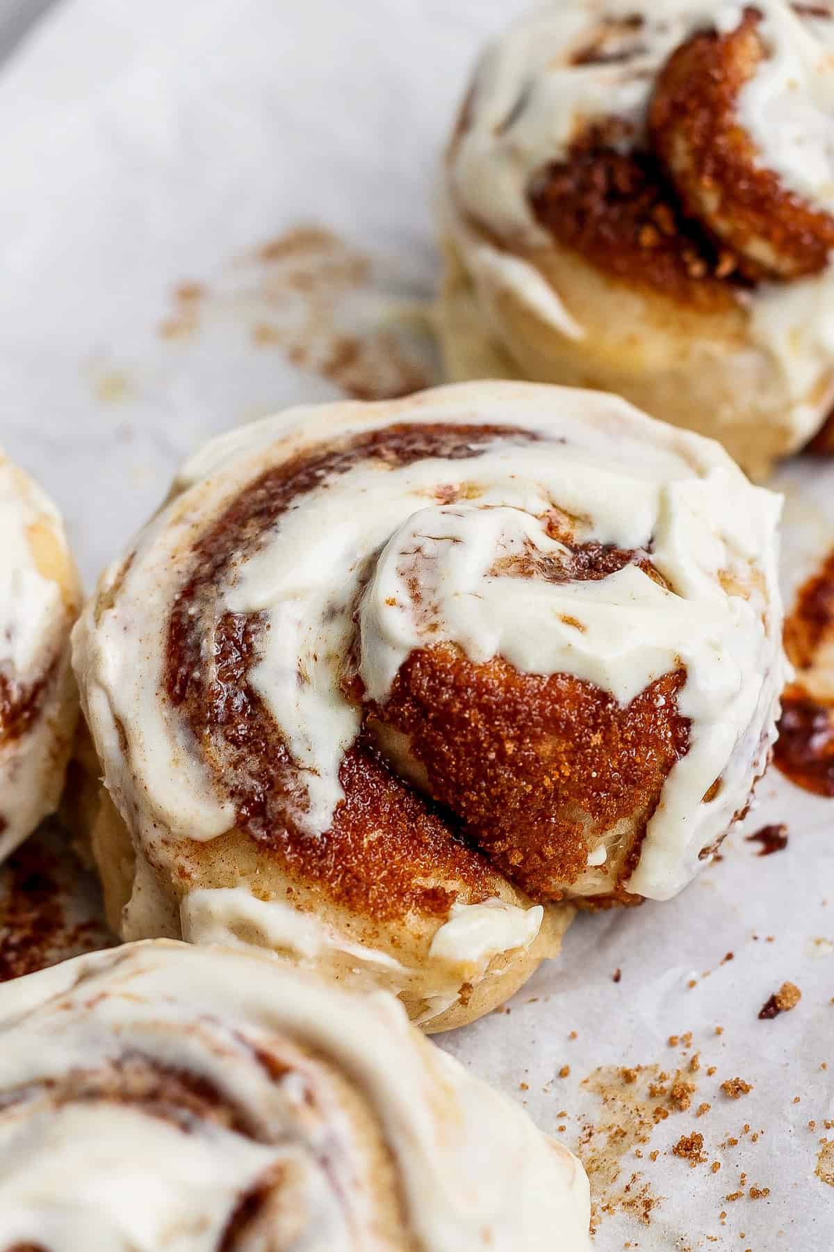 Close-up of protein cinnamon rolls topped with creamy white icing on a parchment-lined surface.