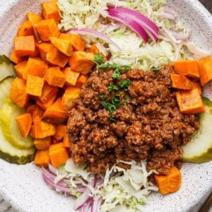 A plate with ground beef, diced sweet potatoes, shredded cabbage, red onions, and pickle slices.