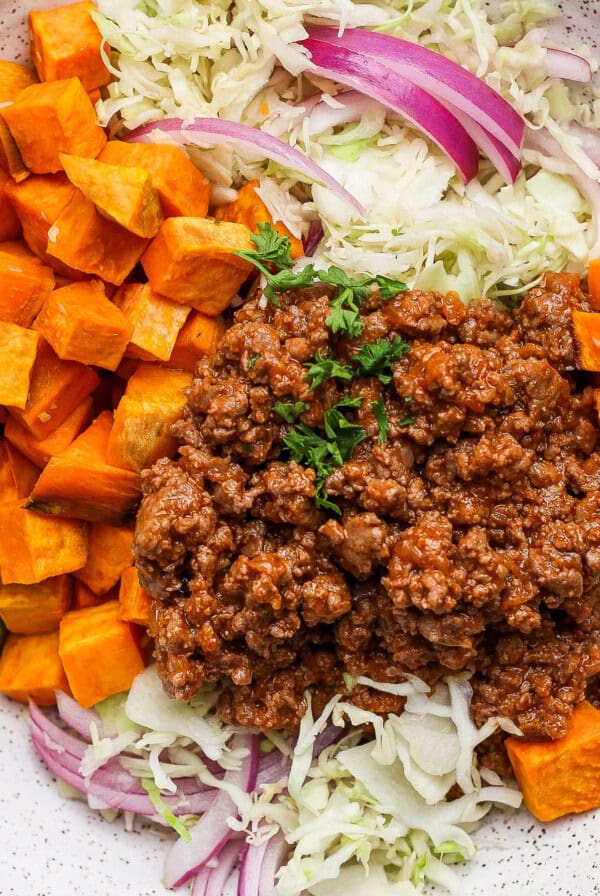 A plate with ground beef, diced sweet potatoes, shredded cabbage, red onions, and pickle slices.