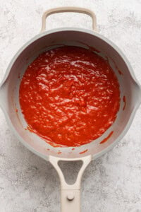 A beige pan filled with red tomato sauce on a gray textured surface.