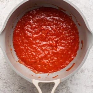 A beige pan filled with red tomato sauce on a gray textured surface.