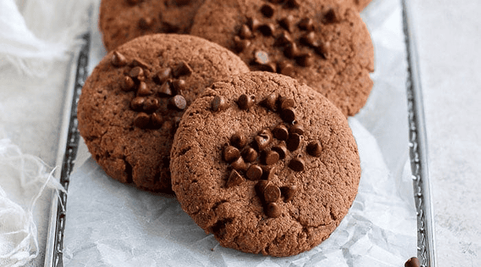 Four chocolate chip cookies on a tray lined with parchment paper.