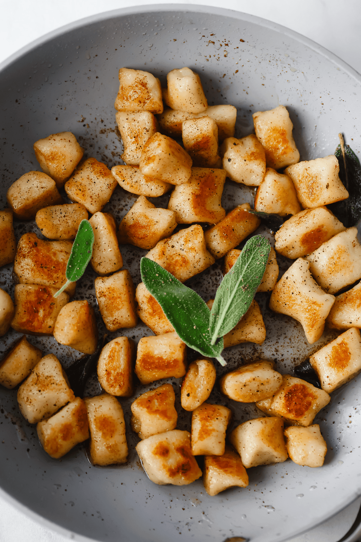 Pan-fried cottage cheese gnocchi with crispy edges, garnished with fresh sage leaves in a gray bowl.