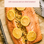 Stuffed salmon with couscous and sun-dried tomatoes, topped with lemon slices, on a baking tray.