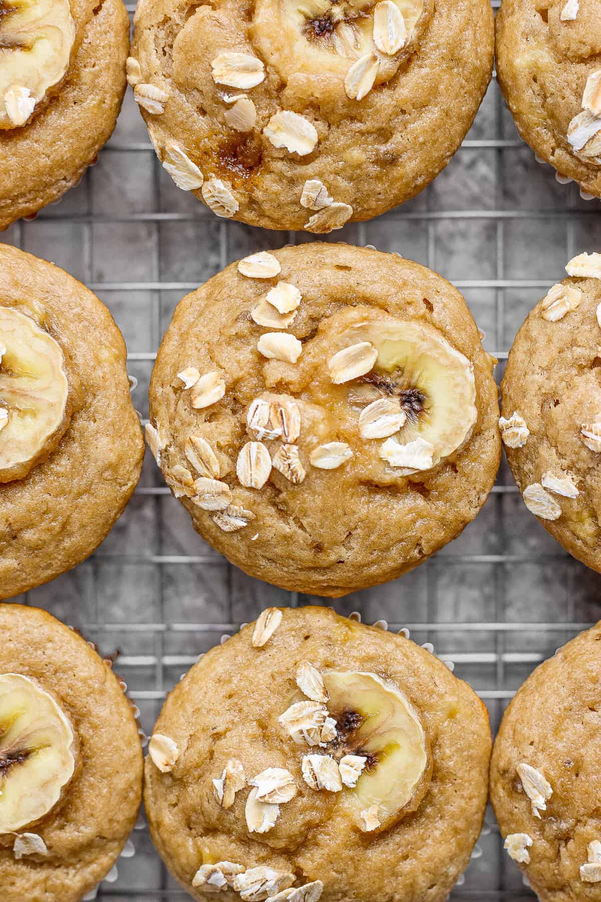 Banana oat muffins on a cooling rack, topped with banana slices and oats.