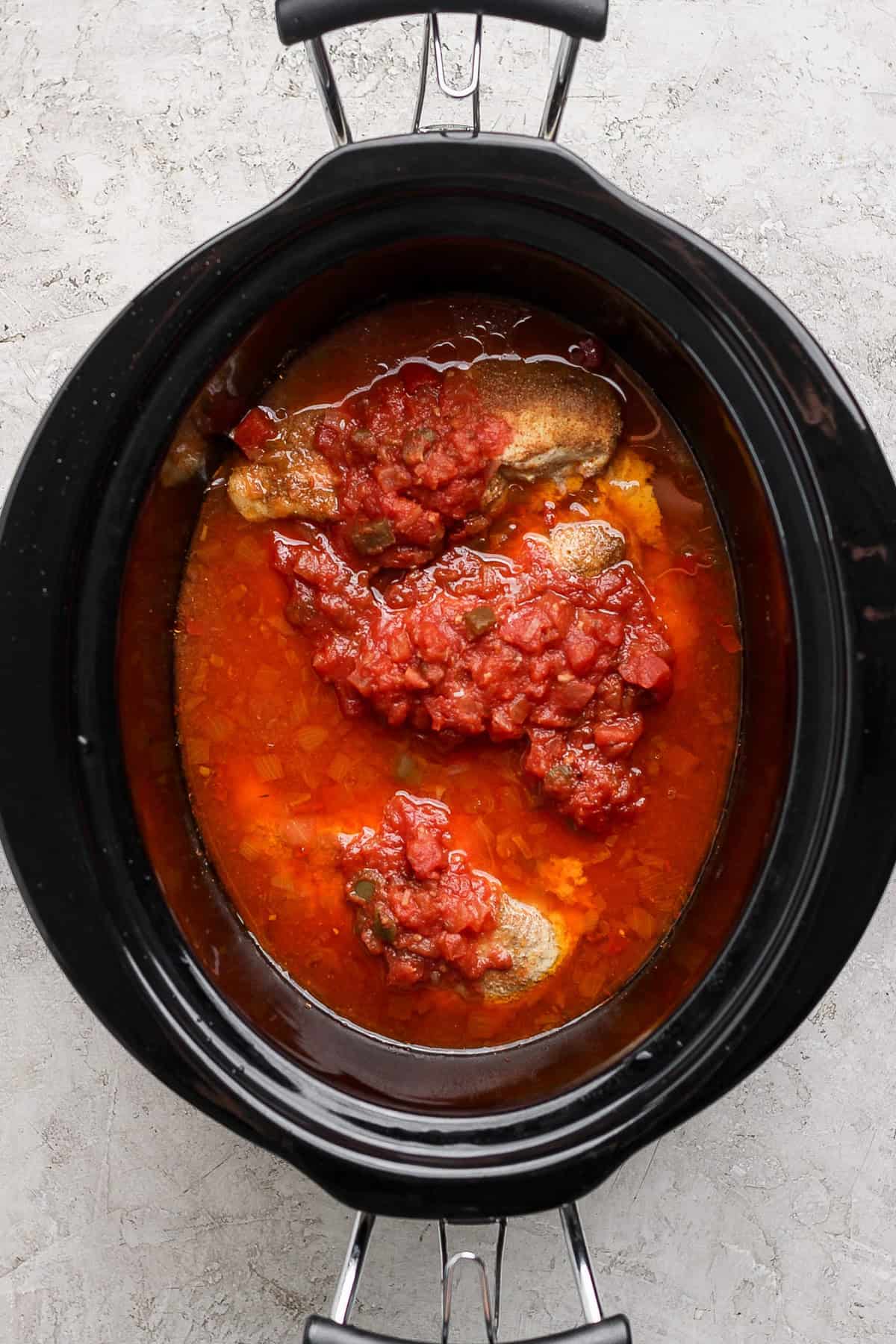 Slow cooker with beef and tomato sauce on a light surface.