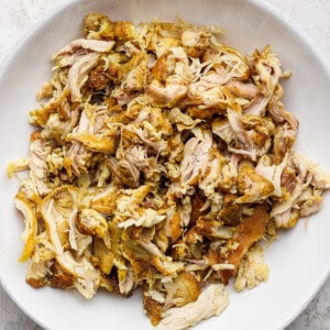 A white bowl filled with shredded, seasoned chicken on a textured surface.