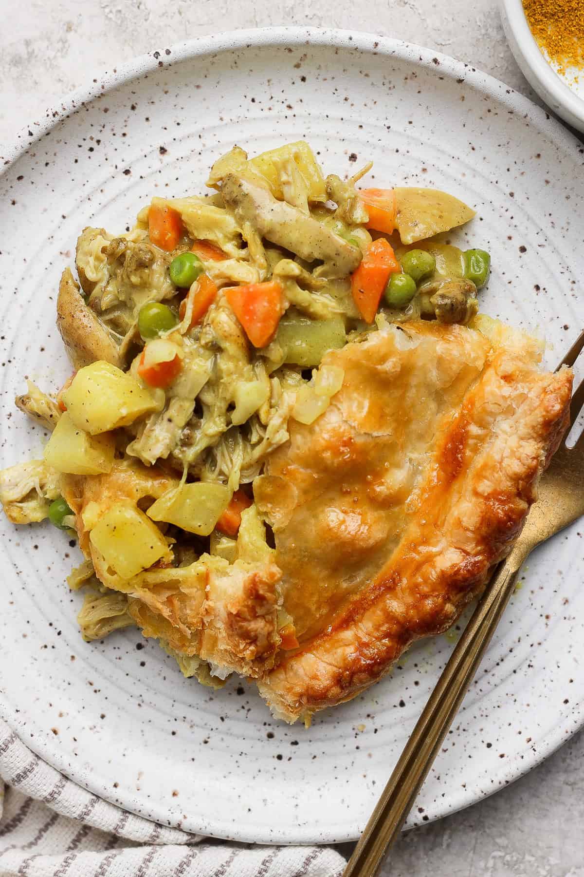 A slice of chicken pot pie with vegetables on a speckled plate, accompanied by a fork and a knife.