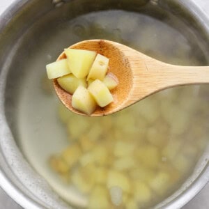 A wooden spoon holds diced potatoes over a pot of boiling water.