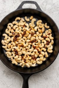 A black skillet filled with roasted cashews topped with a spicy seasoning blend on a textured surface.