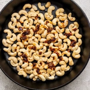 A black skillet filled with roasted cashews topped with a spicy seasoning blend on a textured surface.