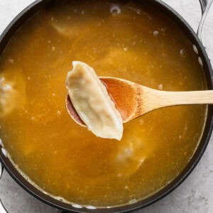 A pot of broth with a wooden spoon holding a dumpling above the liquid.