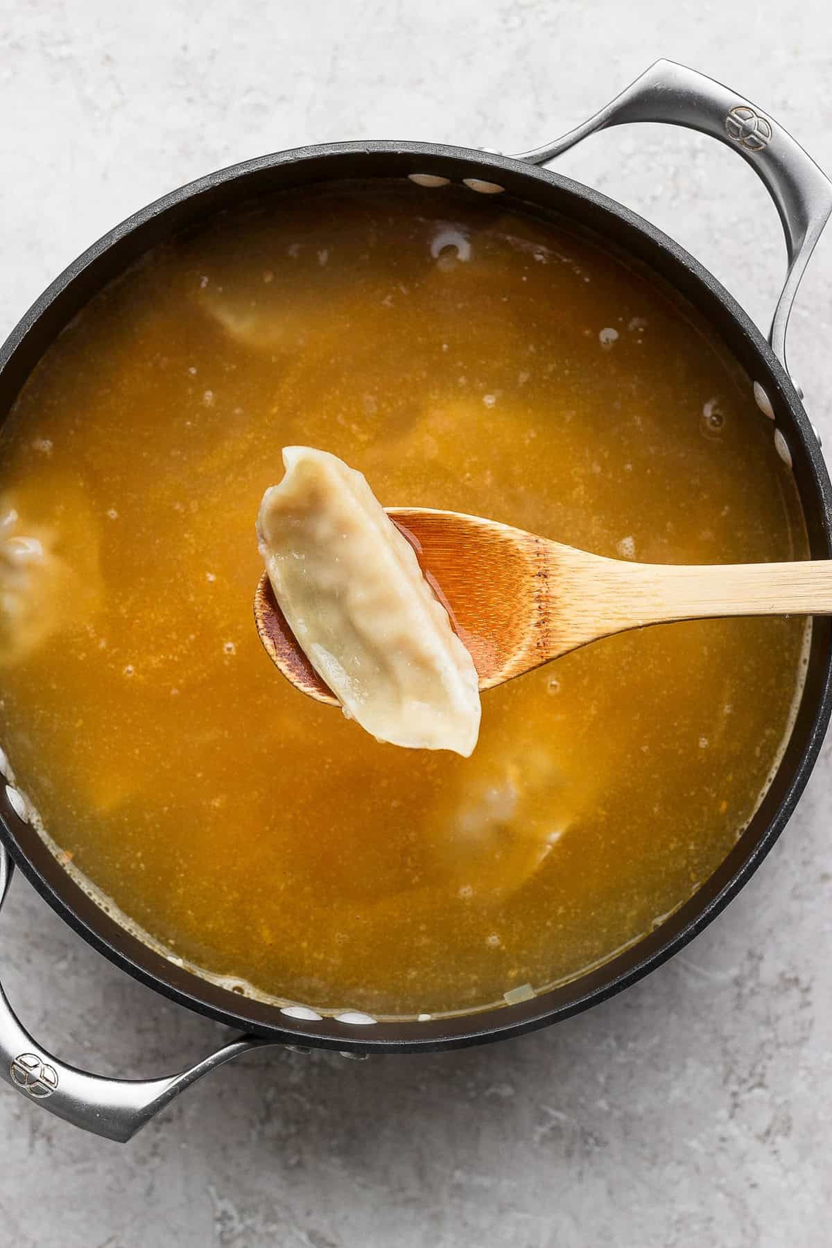 A pot of broth with a wooden spoon holding a dumpling above the liquid.