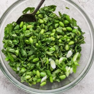 Glass bowl with a green salad containing edamame, chopped cilantro, and sliced green onions, with a metal spoon on the side.