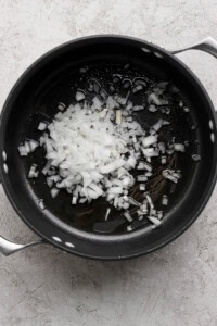 Chopped onions in a black pot on a gray surface.