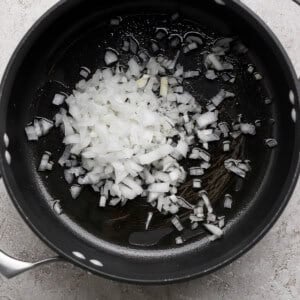 Chopped onions in a black pot on a gray surface.