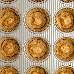 Muffin tray with paper liners filled with unbaked cookie dough, each topped with a dollop of peanut butter.